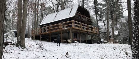 Een blokhut met een houten terras en meerdere verdiepingen, omringd door een besneeuwd bos.