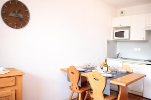 Ein Essbereich mit Holztisch und Stühlen, einer Uhr an der Wand und einer Küche mit weißen Schränken und einer Mikrowelle.