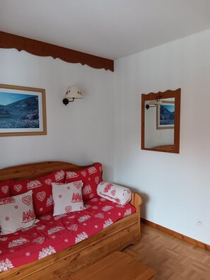 A wooden sofa with red and white patterned cushions, a wall-mounted lamp, and a framed picture of a mountain landscape. - Wifi, Ground floor, swimming pool, balcony, parking, tv, ski locker, 39m², Puy-Saint-Vincent (Puy-Saint-Vincent)