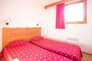 Ein Zimmer mit zwei Betten, jeweils mit einem Holz-Kopfteil, einem Fenster mit rosa Vorhang und einer Wandleuchte.