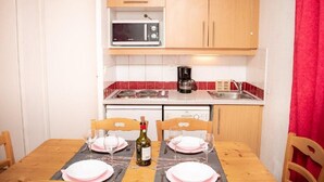 Una cocina compacta equipada con microondas, cafetera y una mesa de comedor para dos personas.