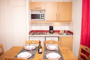 Een compacte keuken met een magnetron, koffiezetapparaat en een eettafel gedekt voor twee personen.