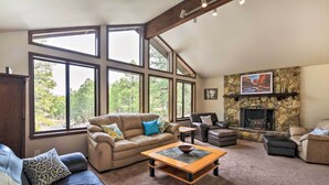 A spacious living room with large windows, a fireplace, and a stone accent wall. - Flagstaff Home w/ Back Deck - 5 Mi to Downtown (Flagstaff)
