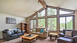 A spacious living room with a large window, a fireplace, and a cozy seating area. - Flagstaff Home w/ Back Deck - 5 Mi to Downtown (Flagstaff)