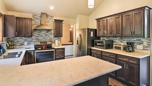 A modern kitchen with dark wood cabinets, a large island, stainless steel appliances, and a stone backsplash. - Flagstaff Home w/ Back Deck - 5 Mi to Downtown (Flagstaff)