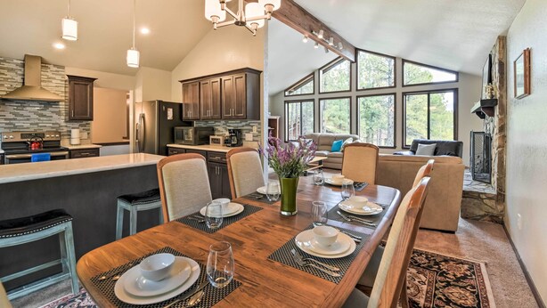 A spacious kitchen with modern appliances, a dining area with a wooden table set for four, and large windows offering natural light and views of the outdoors. - Flagstaff Home w/ Back Deck - 5 Mi to Downtown (Flagstaff)