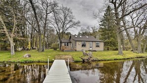 A house with a dock extending into a calm body of water, surrounded by trees. - Lakefront Home w/ Seasonal Dock - 2 Mi to Skiing! (Wautoma)