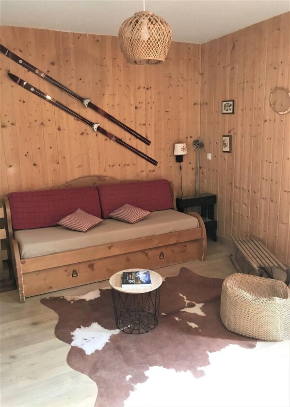 Ein Zimmer mit Holzwänden, einer Couch, einer gewebten Lampe und einem Kuhfellteppich.