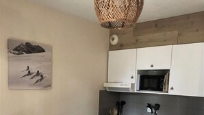 Cozinha compacta com armários brancos, micro-ondas e lava-louças. Inclui uma mesa de jantar com cadeiras e um lustre.