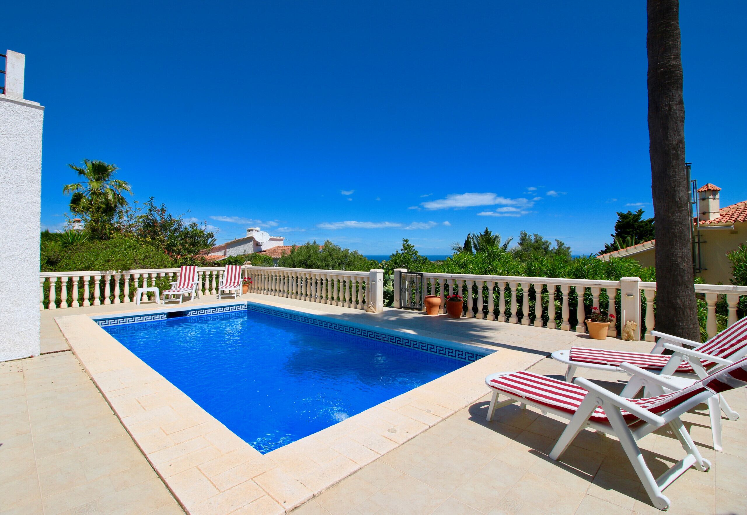 A swimming pool with lounge chairs, a white railing, and a view of the sea.