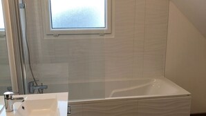 Ein modernes Badezimmer mit einer weißen Badewanne, einem Waschbecken und einer Dusche. Über der Badewanne befindet sich ein Fenster.