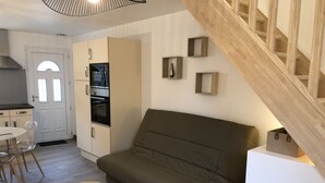 Ein modernes Wohnzimmer mit einer Couch, zwei kleinen Tischen, einer Küchenzeile mit Schränken und Geräten sowie einer Holztreppe.