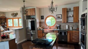 A modern kitchen with a central island, stainless steel appliances, wooden cabinets, and a large window. - Charming Annapolis WaterVIEW Home (Annapolis)