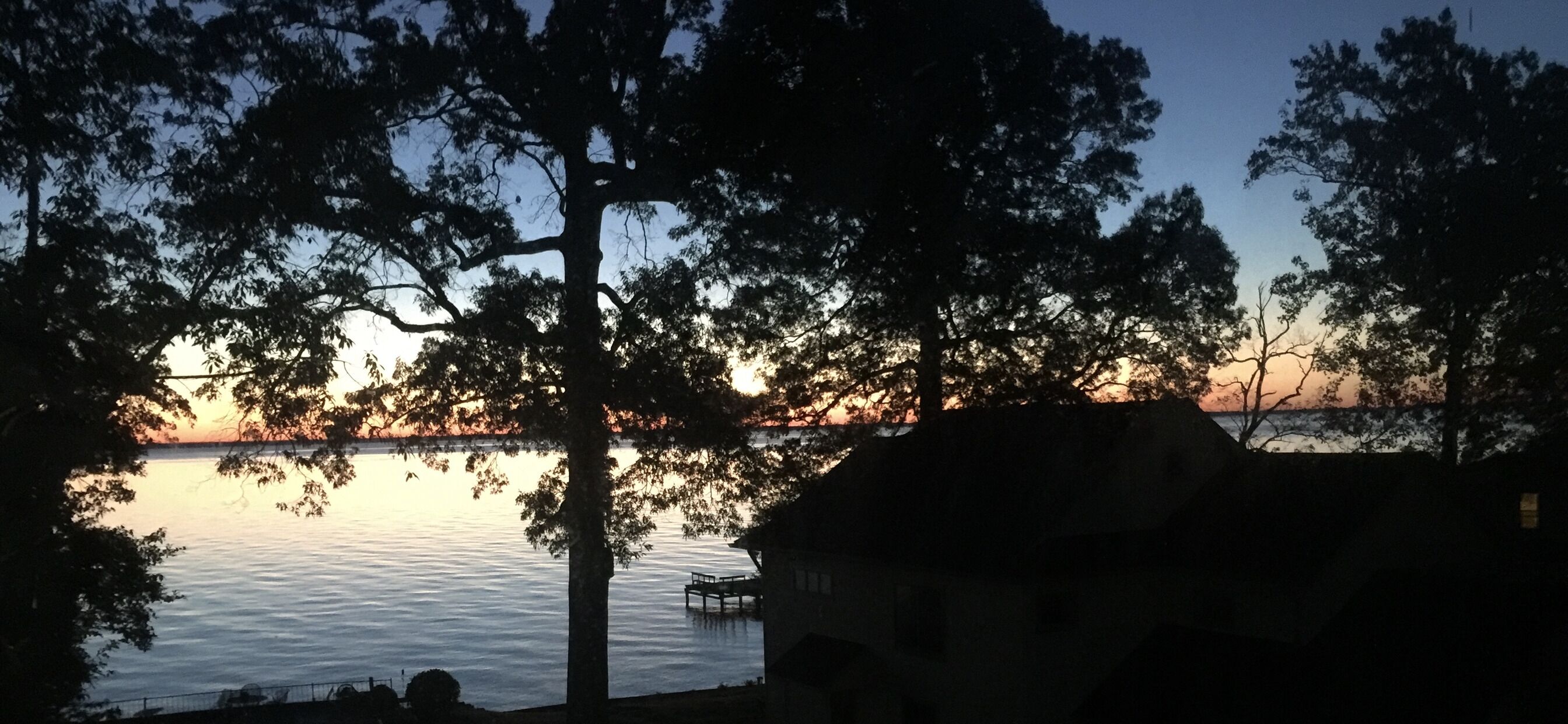 A sunset view over a calm body of water with trees framing the scene.