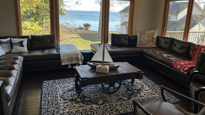 A cozy living room with a large window overlooking a body of water, a leather sofa, a coffee table, and a patterned rug. - Charming Annapolis WaterVIEW Home (Annapolis)
