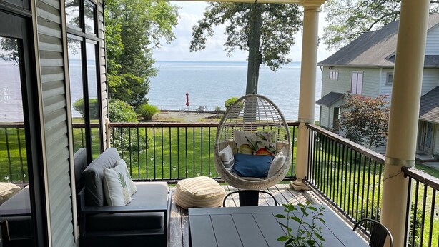 A covered outdoor area with a view of the water, a wicker chair, a table with a plant, and a sofa with pillows. - Charming Annapolis WaterVIEW Home (Annapolis)