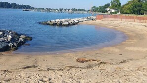 A sandy beach with a calm water body, wooden piers, and a distant shoreline with buildings and trees. - Charming Annapolis WaterVIEW Home (Annapolis)