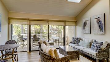A spacious living area with wicker furniture, a glass coffee table, and a balcony with outdoor seating.