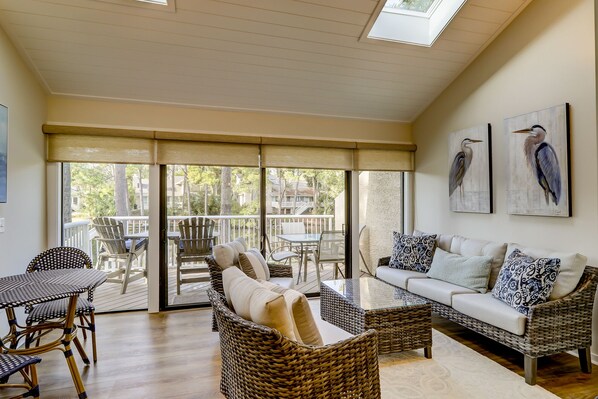 A spacious living area with wicker furniture, a glass coffee table, and a balcony with outdoor seating.