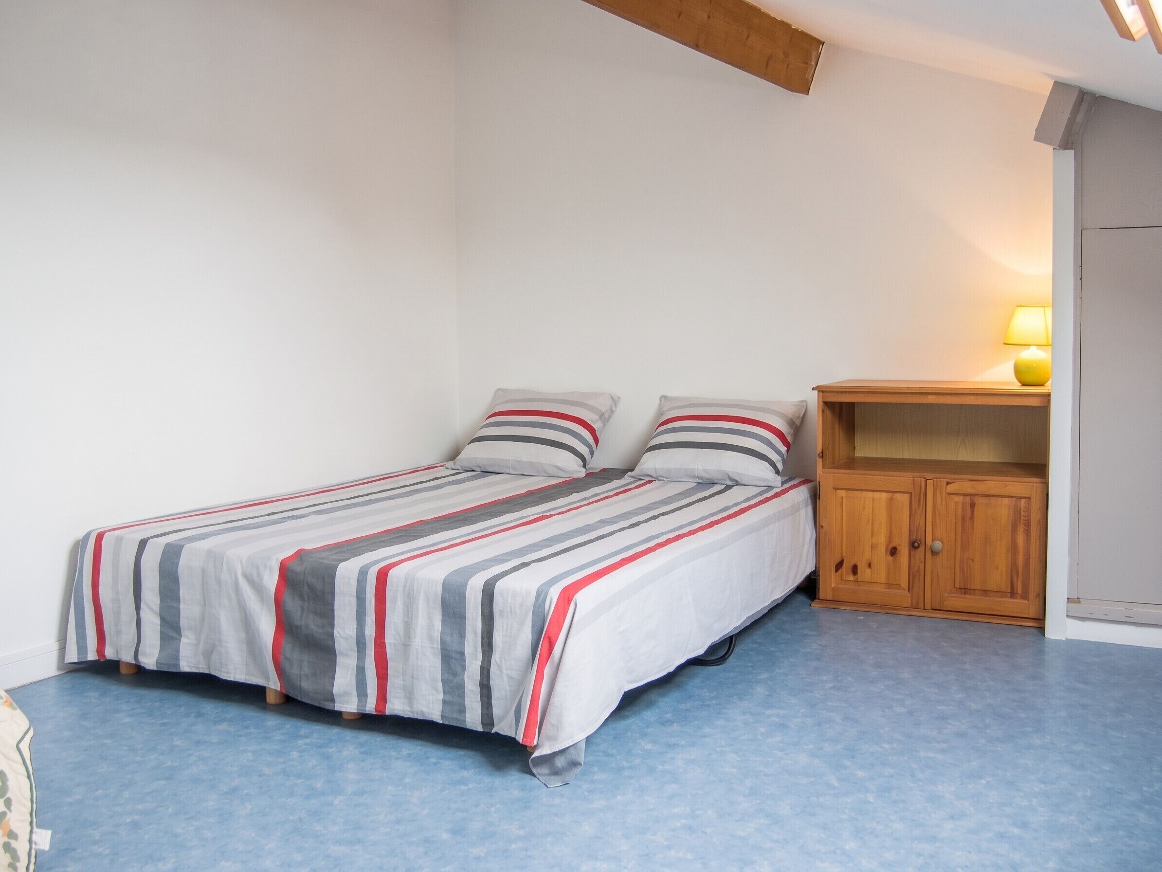Ein Einzelbett mit gestreifter Bettwäsche, ein Nachttisch aus Holz und eine Lampe.