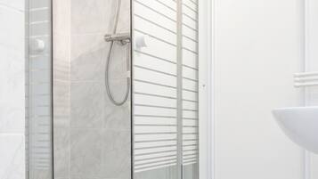 Eine gläserne Dusche mit Duschbrause, eine weiß geflieste Wand und ein Waschbecken mit gebogener Spüle.