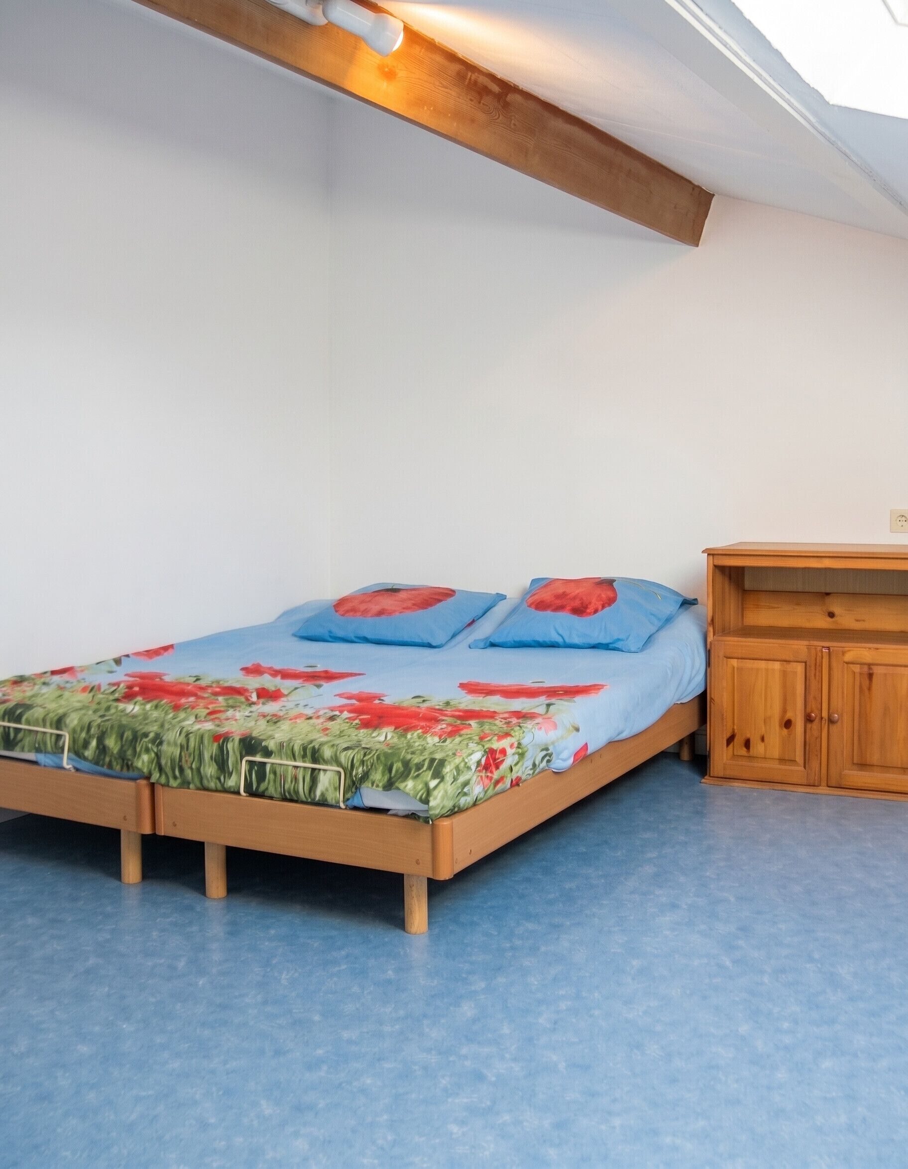 Une chambre à coucher avec un lit en bois, un matelas bleu et une couvre-lit à motifs floraux.