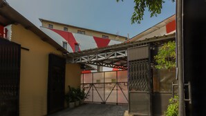 Une cour fermée par un portail en métal, agrémentée de plantes en pot et bordée d’un bâtiment doté d’une marquise rouge et blanche.