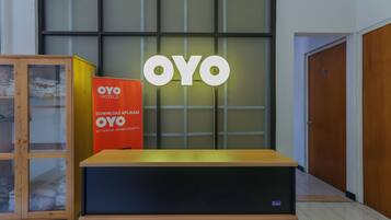 Zona de recepción con un mueble de madera, un letrero rojo de OYO Hotels y un gran letrero iluminado de OYO.