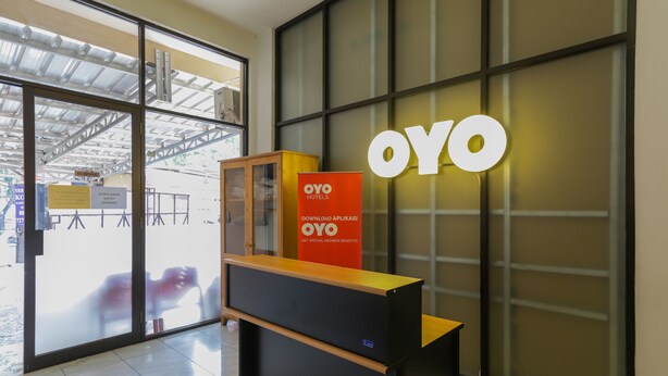 Un comptoir d’accueil avec une enseigne indiquant « OYO Hotels » et une grande enseigne lumineuse « OYO » sur le mur.
