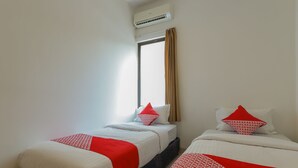 Une chambre d’hôtel avec deux lits, chacun recouvert d’une couvre-lit à motifs rouges et blancs, une fenêtre avec des rideaux beiges et un appareil de climatisation placé au-dessus de la fenêtre.