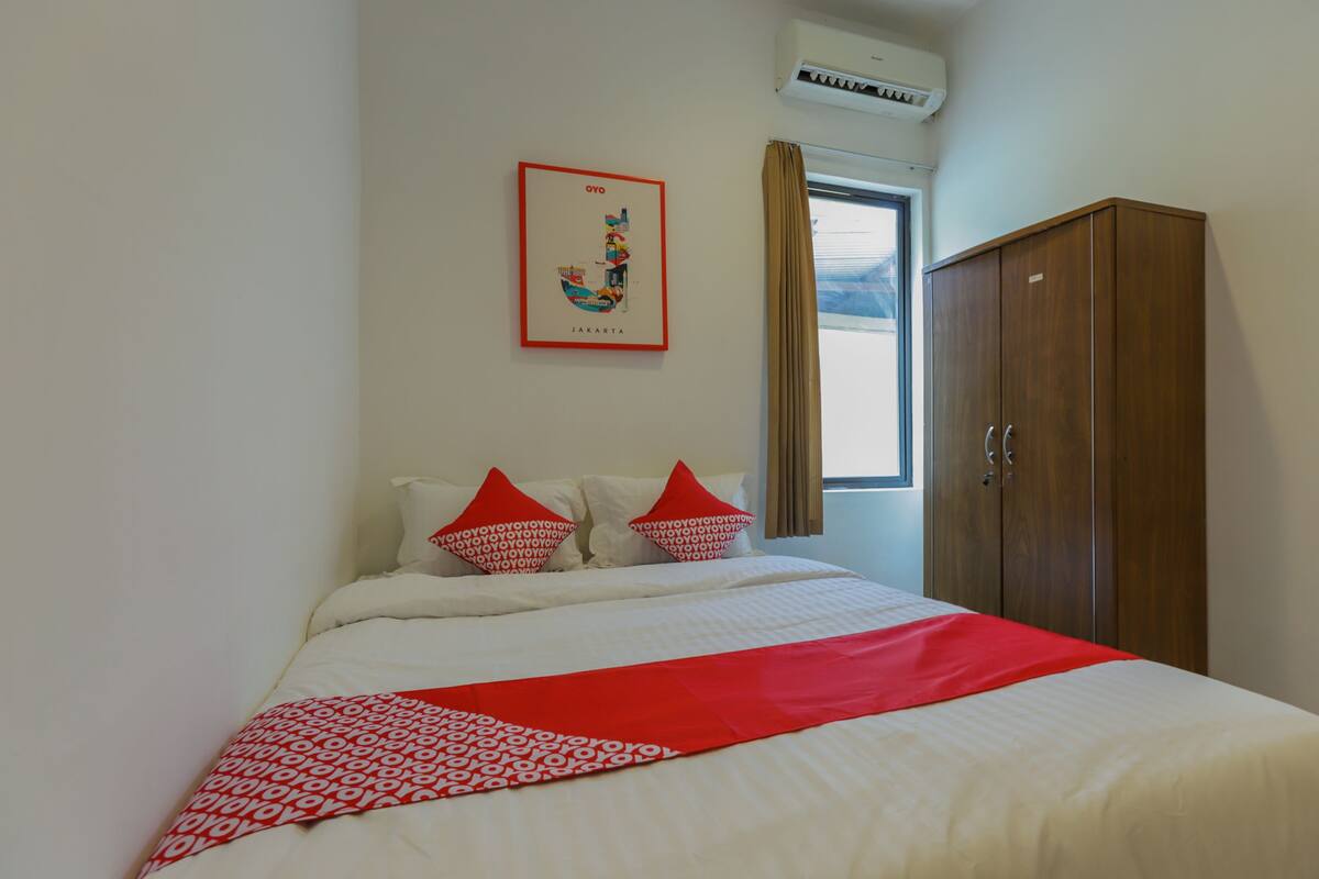 Une chambre d’hôtel comprenant un lit, une armoire, une fenêtre avec des rideaux et un climatiseur fixé au mur.