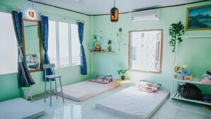 Quarto com duas camas de solteiro, uma cadeira, uma mesinha e uma estante com objetos.
