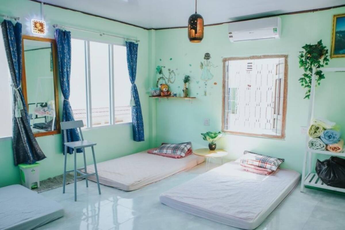 A room with two single beds, a chair, a small table, and a shelf with items.