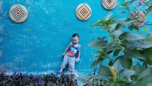 Uma criança em pé sobre uma superfície azul com azulejos decorativos ao fundo.