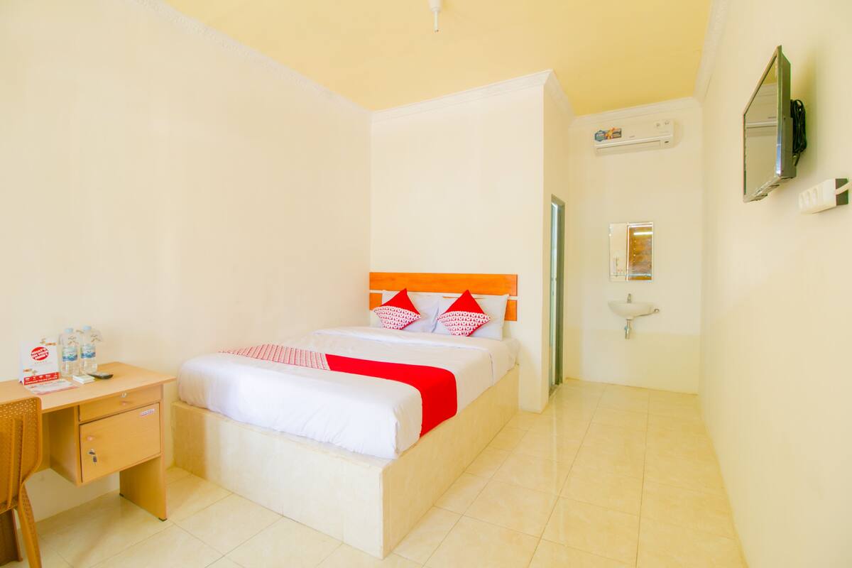 A hotel room with a bed, a desk, a chair, a bedside table, a mirror, a sink, and a television.