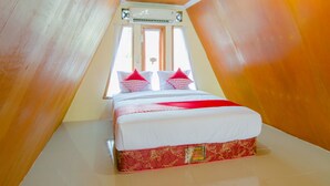 Un dormitorio con techo inclinado, cama con ropa de cama blanca y detalles en rojo, y una ventana con cortinas.