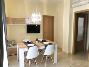 A dining area with a wooden table, white chairs, a flat-screen TV mounted on the wall, and a decorative globe light. - L'APARTAMENT DE LA IAIA. (San Jaime de Enveija)