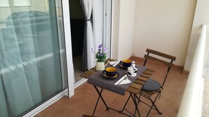 A small balcony with a table set for two, a potted plant, and a chair.