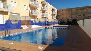 A swimming pool with a tiled deck, surrounded by a low wall and a blue-tiled fence.
