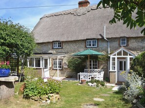 A stone house with a thatched roof, a garden with a bench and umbrella, and a small white door. - 2 bedroom accommodation in Wellow, near Yarmouth (Wellow, near Yarmouth)