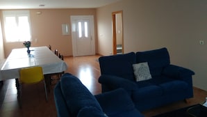 Una sala de estar con un sofá azul, una mesa de comedor con sillas y una puerta que da a otra habitación.