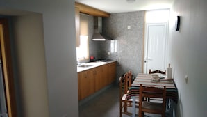 Una cocina compacta con muebles de madera, cocina a gas y zona de comedor con mantel a rayas.