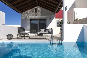 Un área de piscina con sillones de descanso y un porche con paredes de vidrio.