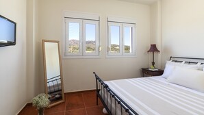 Quarto com cama, mesa de cabeceira, abajur, espelho e duas janelas com vista para as colinas.