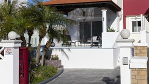 Uma casa moderna de dois andares com fachada branca, telhado vermelho e varanda coberta.