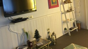 A living room with a flat-screen TV mounted on the wall, a small Christmas tree, a glass coffee table, and a white shelving unit with decorative items. - Elegant independent apartment in the historic center (Vicenza)