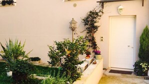 A building with a white facade, multiple windows with wrought iron balconies, a white door, and a small garden area with various plants and a lantern. - Elegant independent apartment in the historic center (Vicenza)