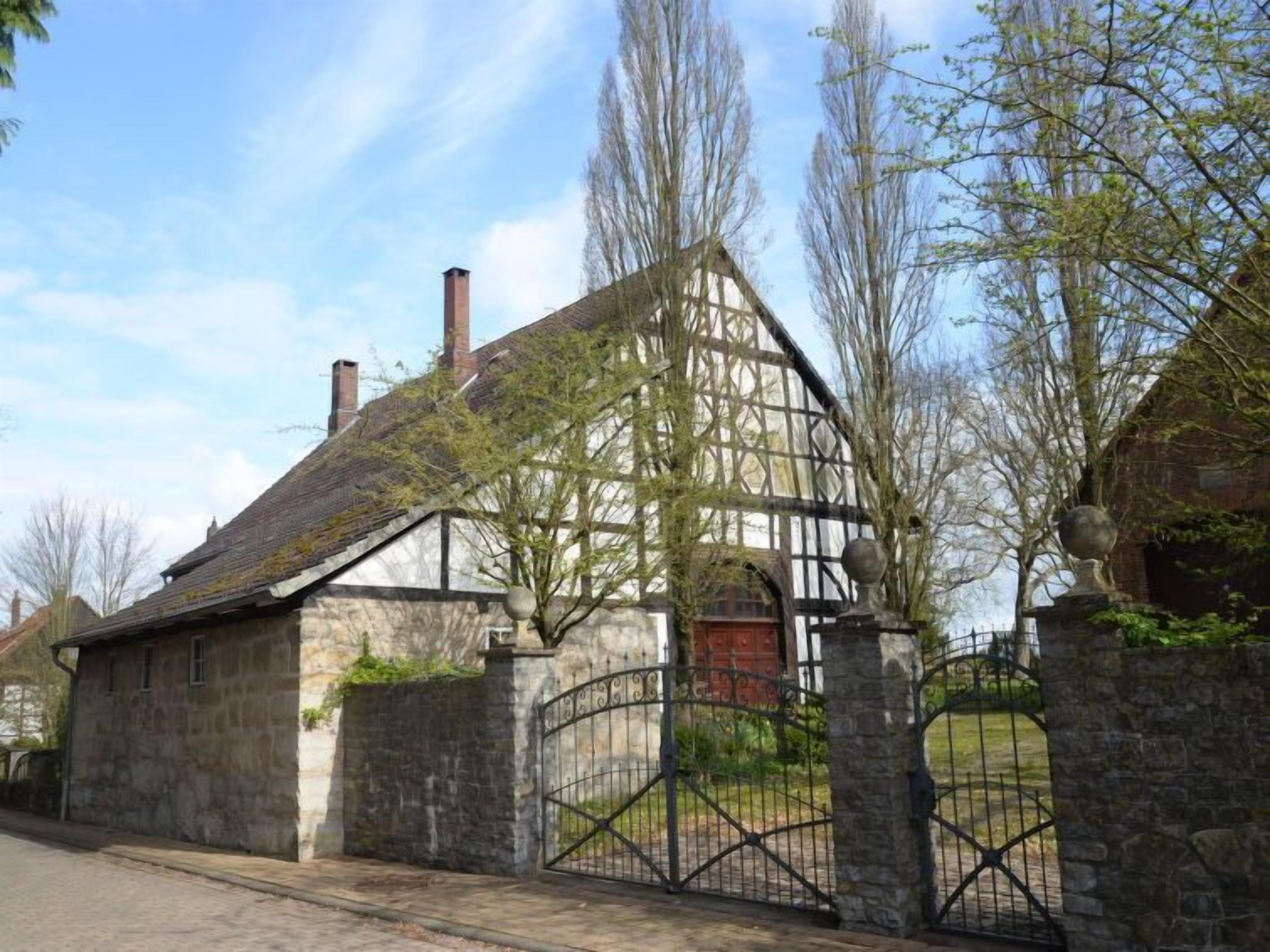 A traditional half-timbered house with a stone wall and a metal gate.