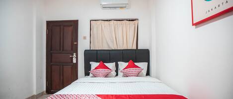A bedroom with a bed, a door, a window with curtains, and an air conditioner on the wall.