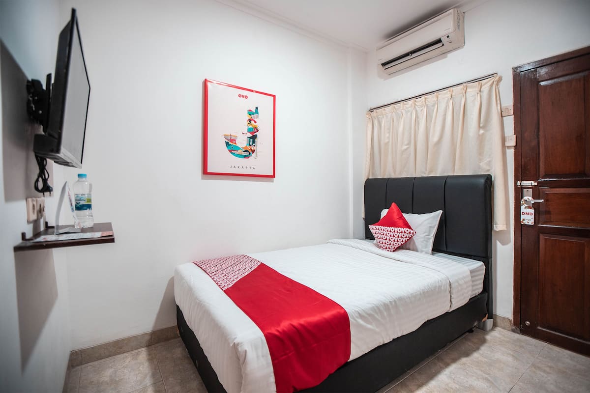 A hotel room with a bed, a TV mounted on the wall, a framed map of Jakarta, and a water bottle on a shelf.